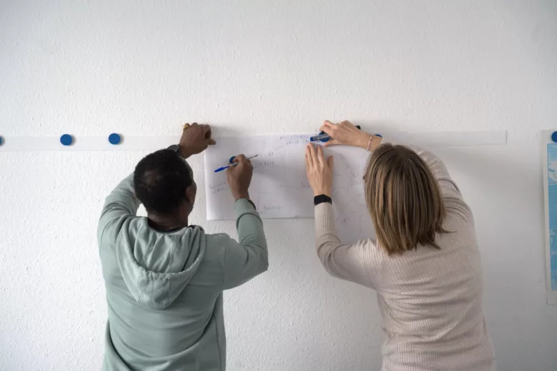 2 Personen die von Hinten gezeigt werden, während sie etwas an einer Wand befestigen